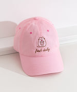 Top-down view of the Pusheen Sweets Cap. The top button and seams can be seen from this view as well as the thread detailing on the bill of the hat. The hat is propped on a white ledge to show the full size of the baseball-style cap. 