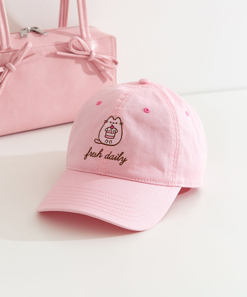 Fresh Daily Pusheen Sweets pink cap. The cat holds a cherry tiered mini cake. 