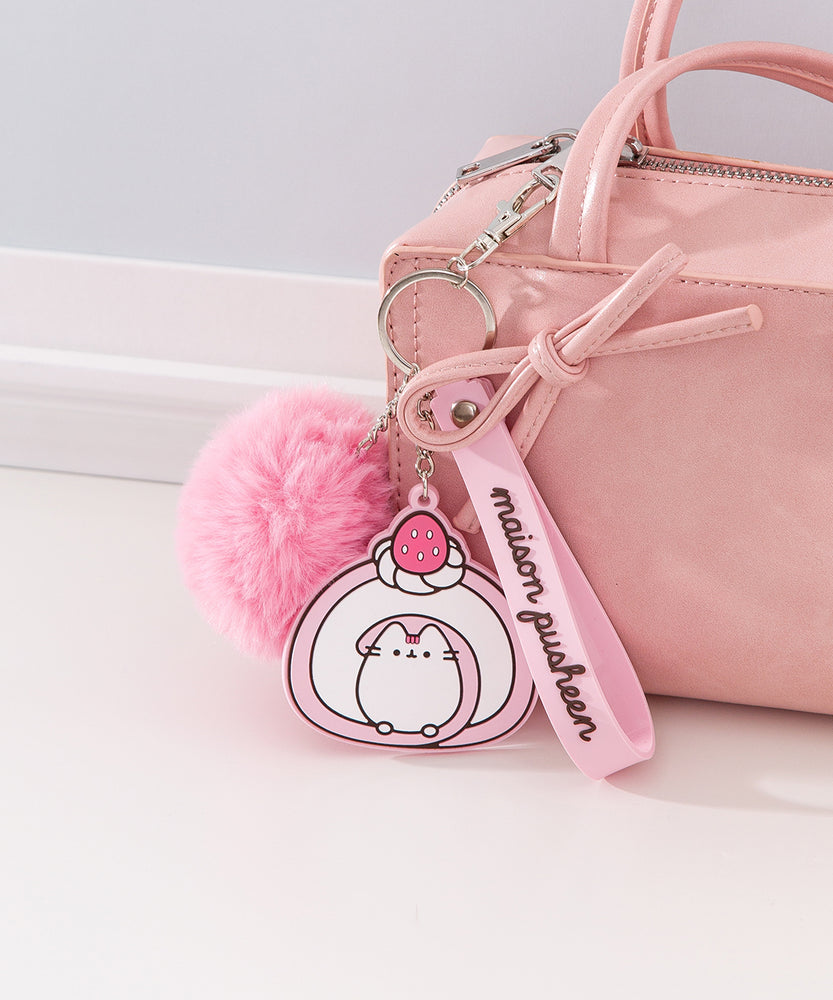 Chunky Pusheen Keychain attached to a pink purse. Pusheen the Cat is transformed inot a pink and white swiss roll topped with a pink and white strawberry and a white whipped cream dollop.