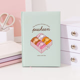 Front cover of the Pusheen Sweets Notebook. On the center of the mint green notebook is a large graphic of Pusheen transformed in four different flavored macarons in a box. The phrases above and below the dessert graphic are "The Society of Little Treats," "pusheen," and "enjoy each day."