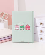 Back cover of the mint green Pusheen notebook. On the center of the back are three graphics of Pusheen the Cat transformed in macarons. On the left is a pink and white vanilla macaron, in the middle is a two-toned green matcha macaron, and on the right is a two-toned pink strawberry macaron. 