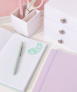 Interior view of mint green notebook. On the white pages are light green writing lines and green graphics of Pusheen as sweet desserts top right corners of the opened pages.