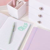 Interior view of mint green notebook. On the white pages are light green writing lines and green graphics of Pusheen as sweet desserts top right corners of the opened pages.