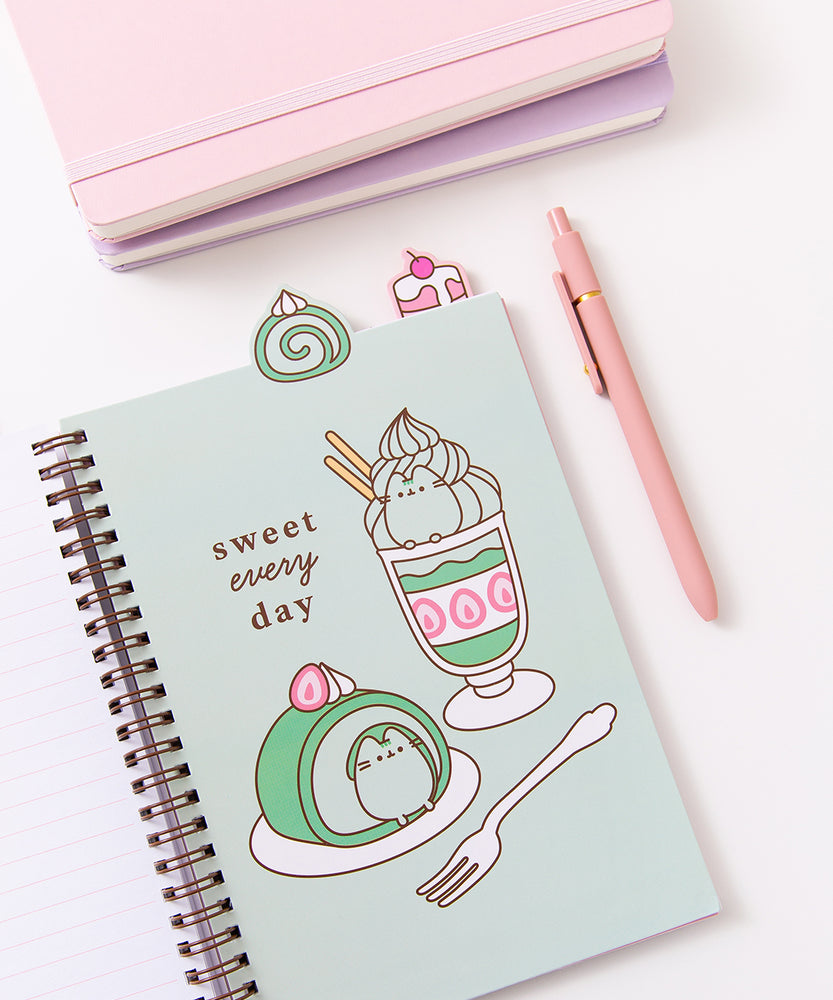 The open notebook shows a green page with a large graphic of a matcha flavored parfait and swiss roll. The green desserts are accompanied by the phrase "sweet every day." Above the notebook are two tabs featuring a matcha flavored swiss roll and a cherry mini cake.
