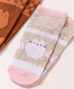 Close-up view of the graphics on the vanilla socks. The white and beige socks have pink accents including Pusheen the Cat in a white color next to some whipped topping piles. 