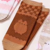 Close-up view of the graphics on the chocolate socks. The two-toned brown socks show Pusheen the Cat in a chocolate color below a brown grid pattern. 
