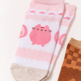 Close-up view of the graphics on the strawberry socks. The white and pink socks have darker pink accents including Pusheen the Cat in a strawberry color next to strawberries. 