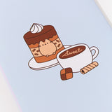 Back of the notebook in the Pusheen Sweets Stationery Set. The light blue notebook has a graphic of Pusheen fitted inside a tiered-mono chocolate cake. Next to the chocolate cake on a plate is a latte with the phrase "sweet."