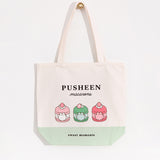 The white canvas bag with pink, green, white, grey, and brown printed graphic hangs on a gold knob in front of a white background. 