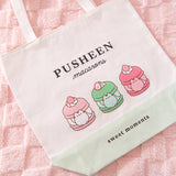 Close-up view of the printed graphic on the front of the Pusheen Sweets Tote Bag. The grey and brown tabby cat is inside three different macarons that are vanilla, matcha, and strawberry flavored.