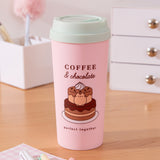 A pink travel mug with a mint green lid. The mug has large graphics on two sides of the cylinder. The front graphic of the Travel Mug shows Pusheen the Cat inside a tiered chocolate cake. The phrase “Coffee & Chocolate” is above the cake graphic while the phrase "perfect together" is below the cake graphic.