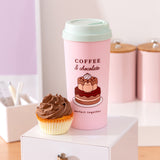 Sweets Pusheen Travel Mug on a desktop with a chocolate cupcake next to the pink Pusheen cup.