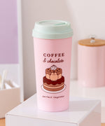Sweets themed Travel mug sits on a desk top. The pink container has large graphics of Pusheen with a chocolate cake. The travel mug comes with a light mint green lid.