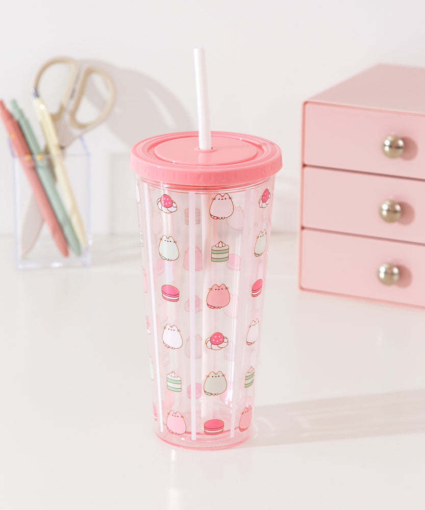 Pusheen water bottle with straw sits atop a desktop. The clear base as light pink hues at the top and bottom of the cup.