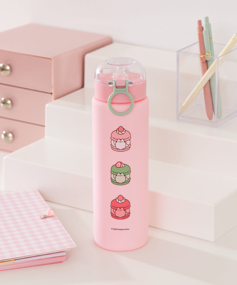 Back view of the Sweets Water Bottle. Descending down the pink bottle are three graphics of Pusheen transformed into macarons. The flavors featured are vanilla, matcha, and strawberry.