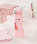 Side view of the Pusheen Sweets Water Bottle. The clear flip-top lid is closed while the mint green carrying handle is up. The pink water bottle has designs of Pusheen transformed into strawberry, vanilla, and matcha macarons.