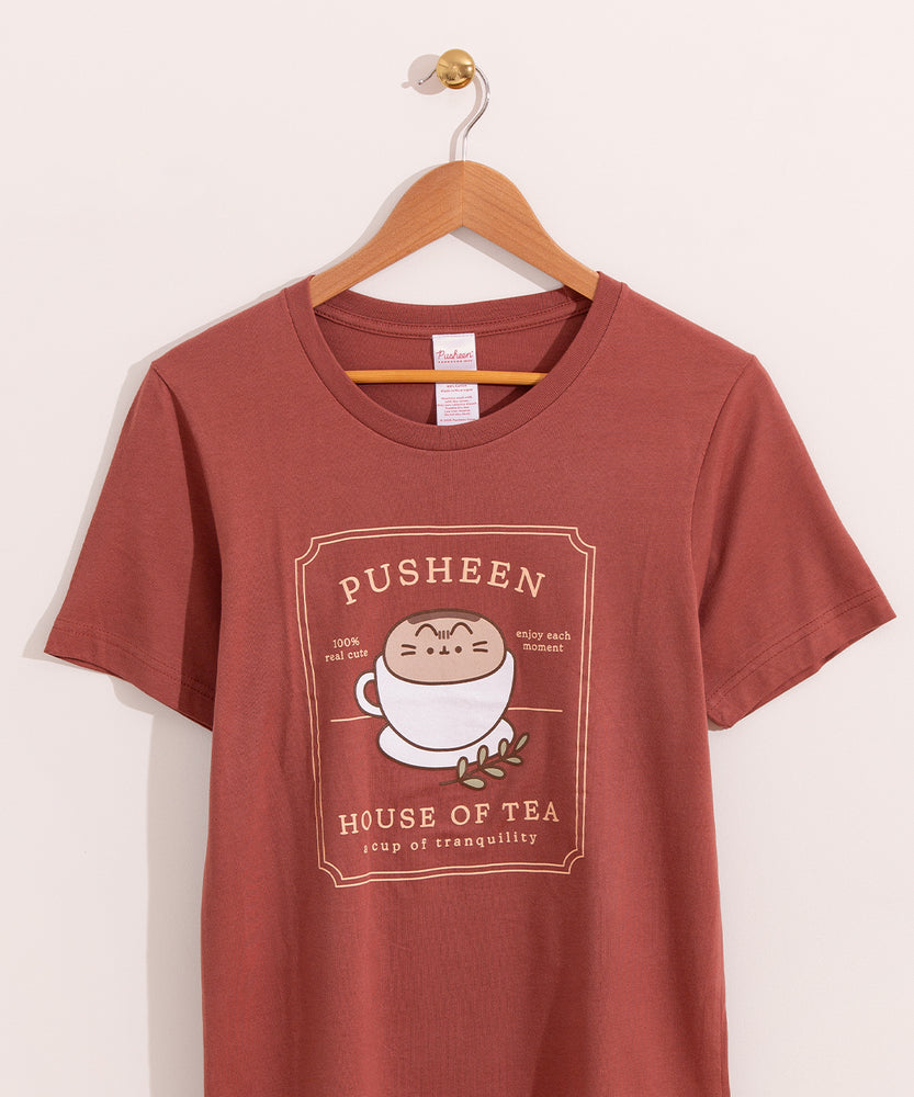 Rustic red t-shirt with a large graphic on the front center. The graphic shows Pusheen the Cat nestled in a tea cup on a saucer with a leaf sprig next to the cup.