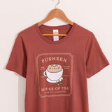 Rustic red t-shirt with a large graphic on the front center. The graphic shows Pusheen the Cat nestled in a tea cup on a saucer with a leaf sprig next to the cup.