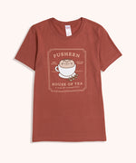 Tea t-short lies on a flat surface. The red tee has a large graphic in the center front of the t-shirt feauring Pusheen the Cat nestled inside a tea cup giving her body an extra round appearance. 