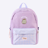 A purple backpack featuring Pusheen saying "stay cool." The backpack features a front zip-up pocket with a purple grid pattern. The main portion of the backpack is a plain purple color.