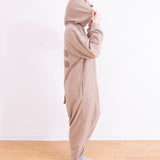Model faces to the side while wearing the Pusheen Kigurumi Onesie. The model holds up the hood with their hands so that the felt ears can be seen sticking up. In this view, the back stripes and tail details can be seen. 