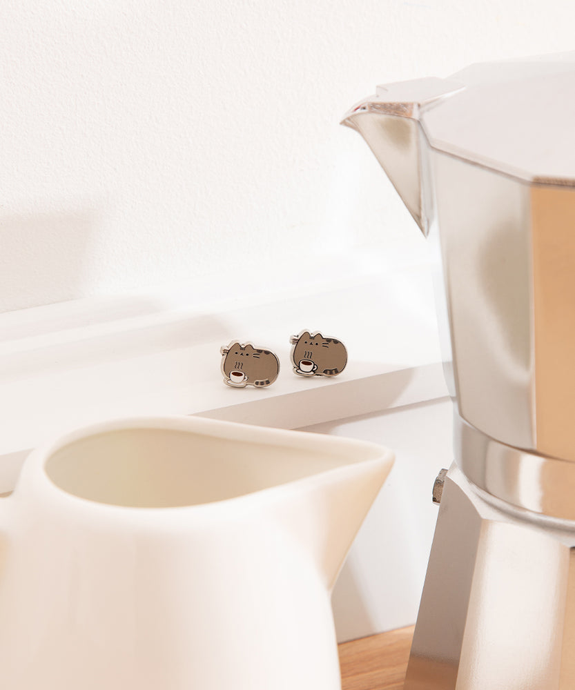 Pusheen Coffee Stud Earrings show Pusheen the Cat with a steaming coffee mug. The earrings are outlined in silver.