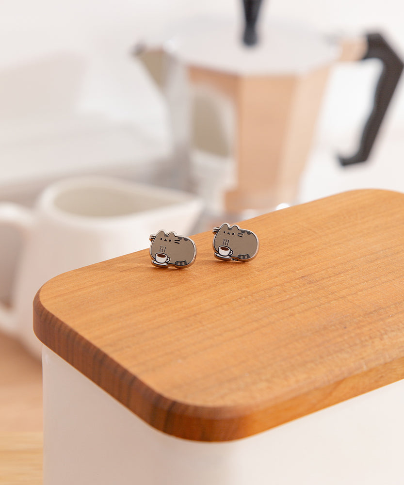 Pair of small cat-shaped earrings on a wooden surface with a blurred background