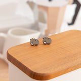 Pair of small cat-shaped earrings on a wooden surface with a blurred background