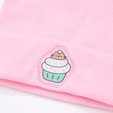 Close-up view of embroidered patch on the Pusheen Cupcake Knit Hat. Pusheen sits in sprinkled cupcake. Pusheen is shown in her classic grey colors and brown whiskers. 