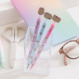 Three pens with Pusheen the Cat tops in a clear holder on a light surface.
