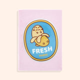 Front cover of the Pusheen Fruits Plush Notebook. On the center of the pink notebook is a PVC patch of Pusheen the Cat as a yellow banana in front of a blue background with a yellow border. Under the banana graphic is the word "Fresh" and the banana grocery code "#4011."