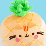 Aerial view of the Pineapple plush. The vibrant green crown has different layers of leaves to mimic a real pineapple stem. Pusheen’s face includes her classic three head stripes, eyes, mouth and whiskers plus light pink blush spots near her mouth. 