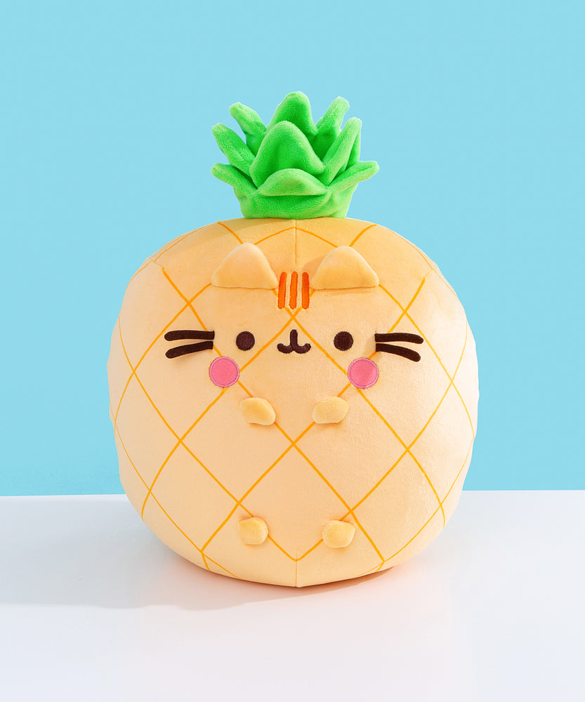 Front view of the Pusheen Fruits Scented Pineaplle Squisheen Plush. Pusheen the Cat is a yellow pineapple with a vibrant green crown that’s sitting atop a white tabletop.