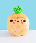 Front view of the Pusheen Fruits Scented Pineaplle Squisheen Plush. Pusheen the Cat is a yellow pineapple with a vibrant green crown that’s sitting atop a white tabletop.