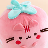 Aerial view of the Strawberry plush. The light green stem has four leaves to mimic a real strawberry. Pusheen’s face includes her classic three head stripes, eyes, mouth and whiskers plus light pink blush spots near her mouth. 