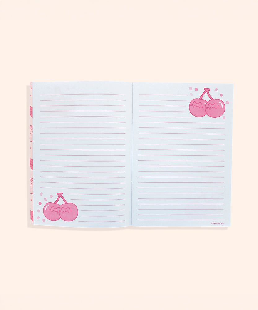 Interior view of a writing page in the notebook. The pink lined white pages feature light pink and red graphics of Pusheen as a pair of cherries on stems surrounded by confetti.