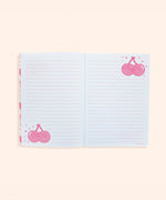 Interior view of a writing page in the notebook. The pink lined white pages feature light pink and red graphics of Pusheen as a pair of cherries on stems surrounded by confetti.