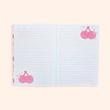 Interior view of a writing page in the notebook. The pink lined white pages feature light pink and red graphics of Pusheen as a pair of cherries on stems surrounded by confetti.