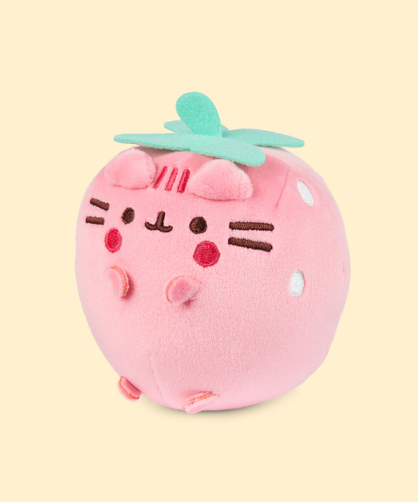 Left quarter view of the light pink-colored Pusheen Squisheen. In this angle, Pusheen’s triangle ears can be seen coming off the light pink round plush body. 