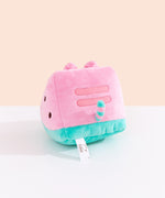 Side and back view of the Watermelon Fruit Plush. On the sides are brown circles to mimic watermelon seeds. On the back of the plush are embroidered red stripes to mimic Pusheen’s classic back stripes. Extending off the bottom back of the Pusheen is a pink and green striped tail. 
