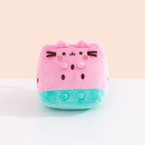 Front view of the Pusheen Fruits Watermelon Plush. Pusheen the Cat takes the form of a triangular watermelon slice. The pink and green plush sits atop a white tabletop. 