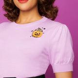 Close-up of Pusheen and Jack-O-Lantern embroidery on wearer’s left chest. A greyPusheen sits in an orange and black Jack-O-Lantern with a top of the pumpkin and stem sitting on her head as a hat. The cat is surrounded by five black stars. 