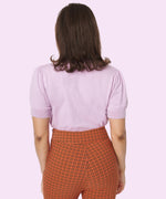 Model shows off the back of the Pusheen Halloween Knit Sweater. The lavender knit sweater does not have any embroidery graphics on the backside. The knit sweater is paired with orange and black plaid pants. 