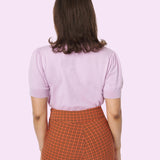 Model shows off the back of the Pusheen Halloween Knit Sweater. The lavender knit sweater does not have any embroidery graphics on the backside. The knit sweater is paired with orange and black plaid pants. 