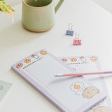 Two purple and white notepads on a desktop. The lined pages include a pink checkbox on each line.