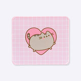 Front view of the Pusheen Mouse Pad. The pink pad has a white grid pattern all over. In the middle of the rectangle is a graphic of a blushing gray cat leaping inside a large pink heart.
