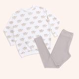 The Pusheen Patterned Loungewear Set lies on a yellow background. The set includes a cream-colored tunic top with an all over print of Pusheen the Cat in her classic grey and brown coloring. The set also includes taupe-colored legging bottoms that are folded in this image. 