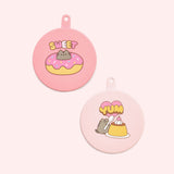 Close-up of the pink can covers where one is dark pink and one is light pink. The two silicone can covers have graphics printed on the top of Pusheen with sweet treats including a donut and flan.
