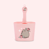 Pink litter scoop and scoop holder have Pusheen the Cat designs with roses. The scoop holder has a ledge to hang over the box.