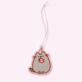 Front view of 1 of the 2-pack of Pusheen Air Fresheners. A strawberry-scented Pusheen graphic of a blushing cat holding a pink strawberry hangs on a pink elastic string. 